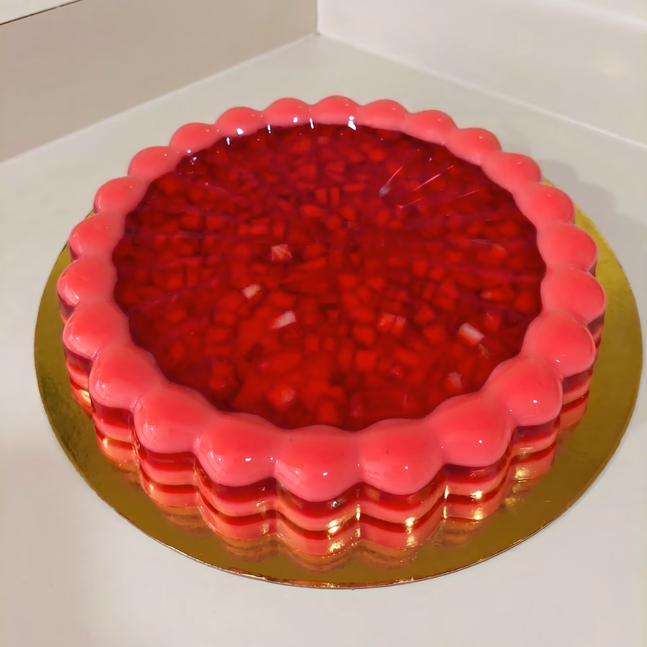 Gelatina redonda festoneada, rosada, con cubitos de fresa en su capa superior transparente