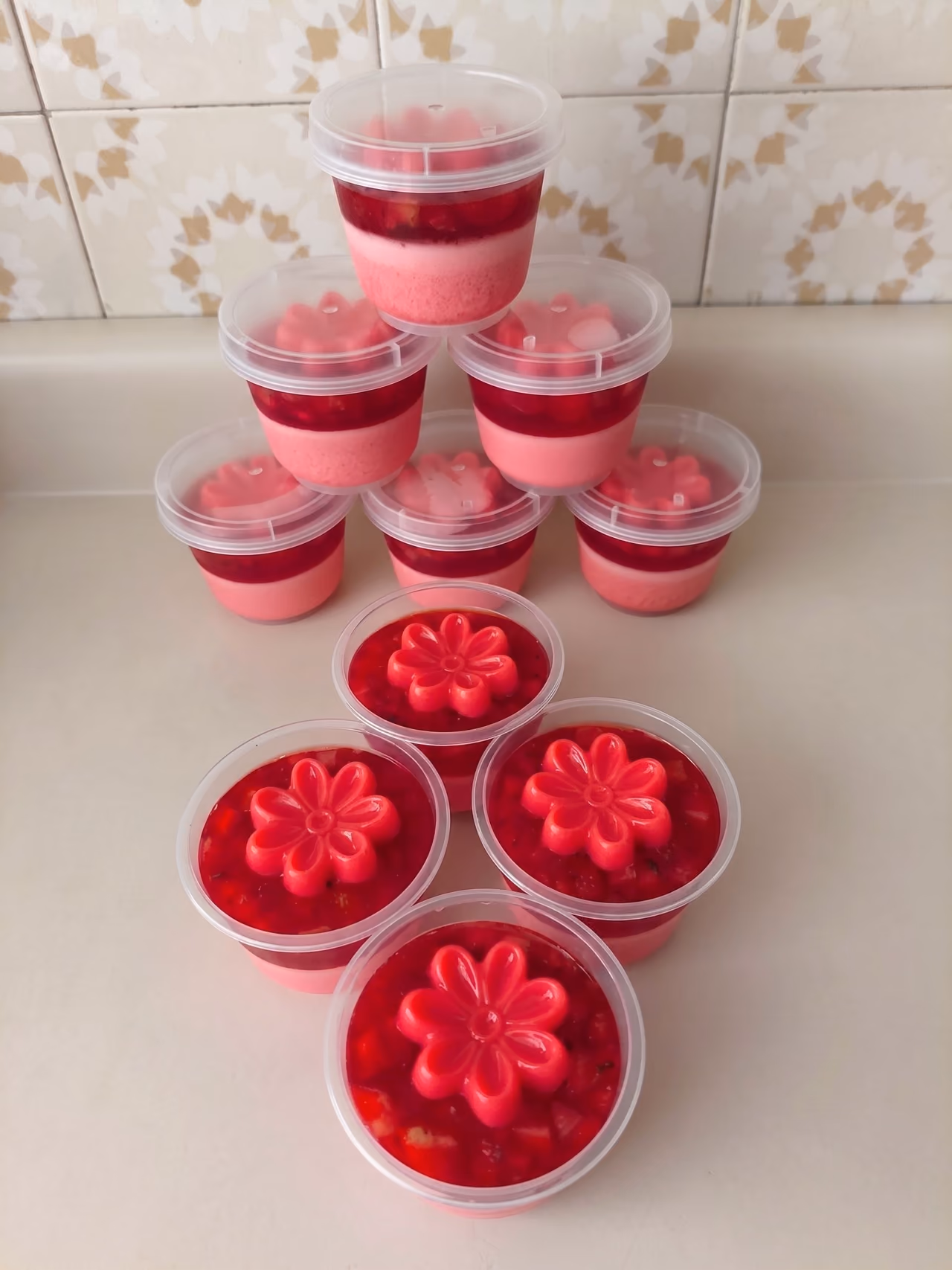 Envases individuales con tapa de gelatina de fresa, con cubitos de fruta y una flor rosada encima