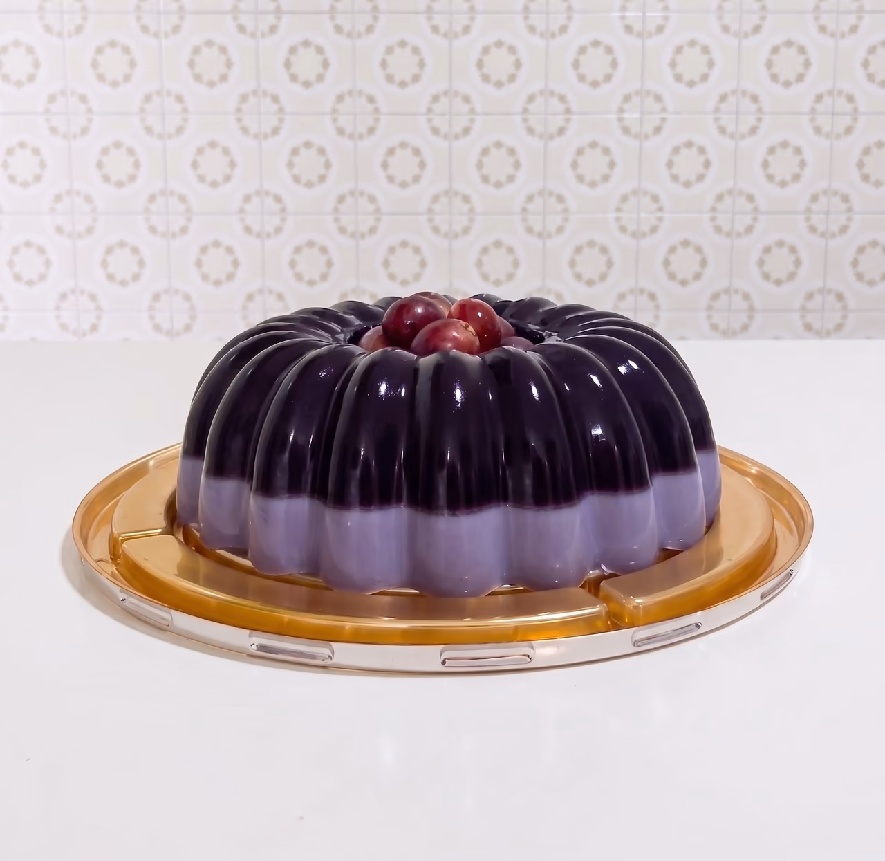 Gelatina en molde acanalado, morada oscura sobre capa lila, con uvas en el centro